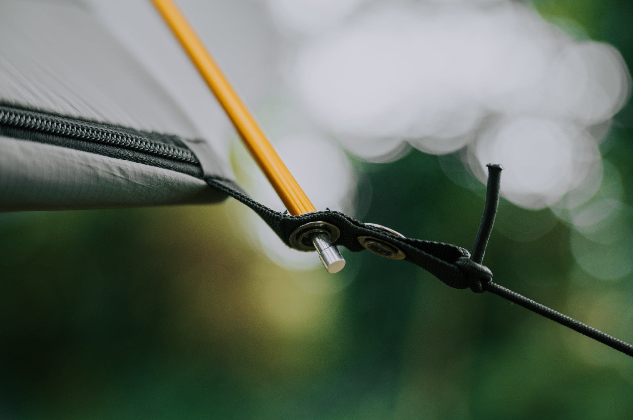 Close-up of the grommet where the spreader pole is inserted into the Crua Culla Hammock Wrap, showcasing build quality with a blurred tree line in the background.