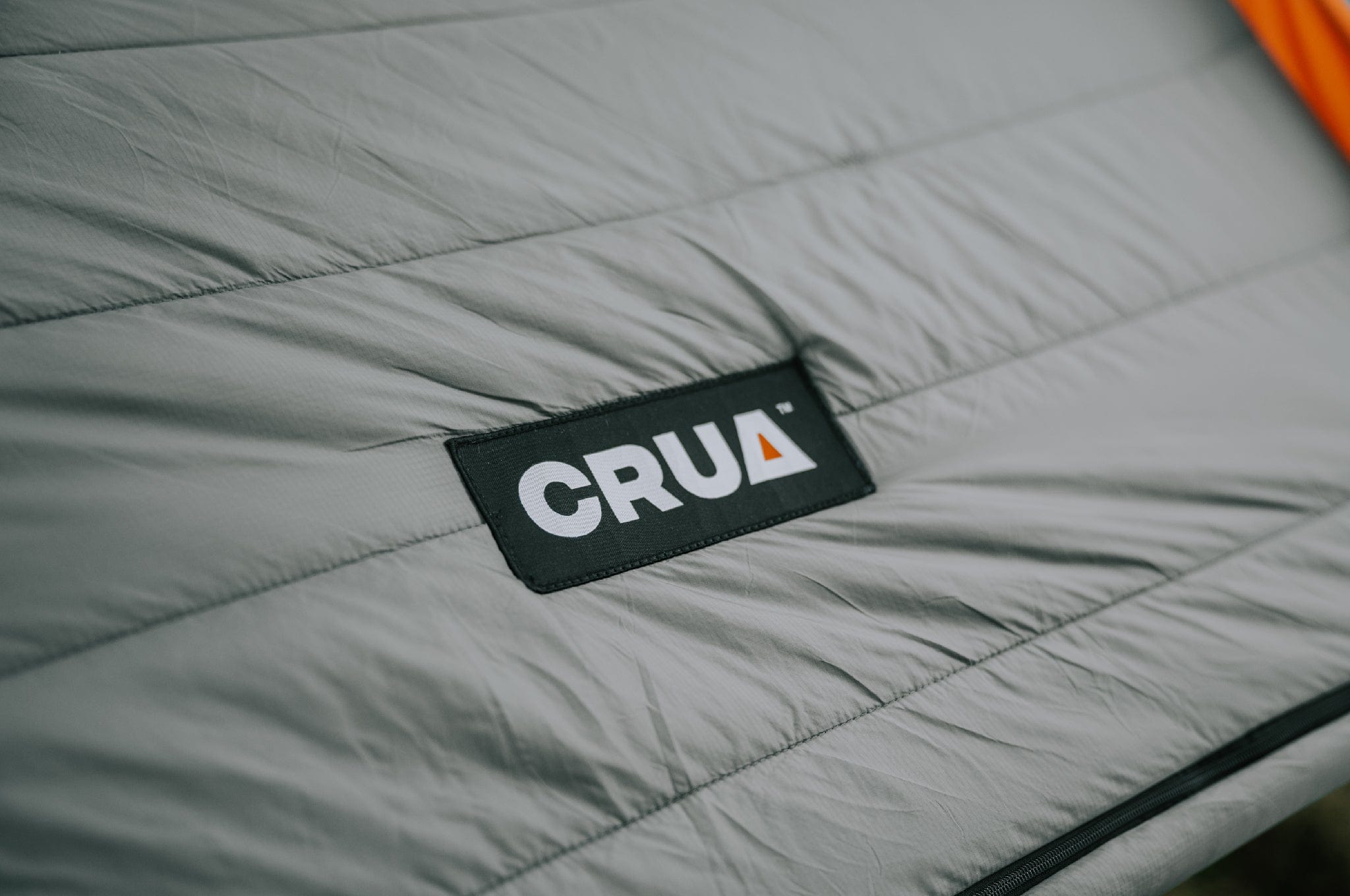 Material close-up of the Crua Culla Hammock Wrap, featuring the embroidered Crua logo badge in the center of the shot.