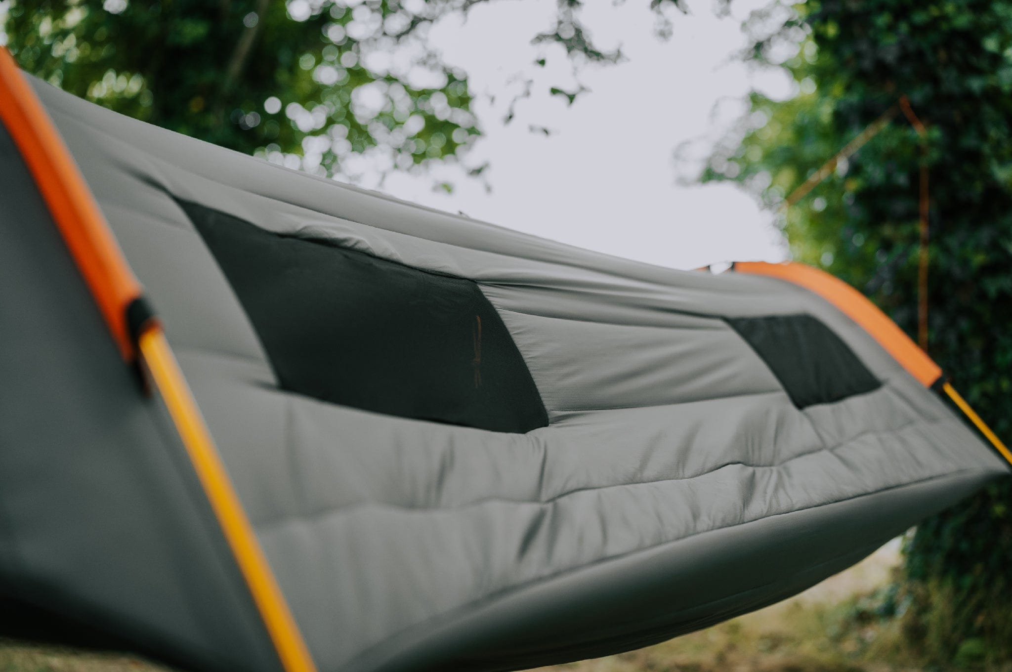 Close-up side view of the Crua Culla Hammock Wrap, looking down its length with mesh windows and trees in the background.