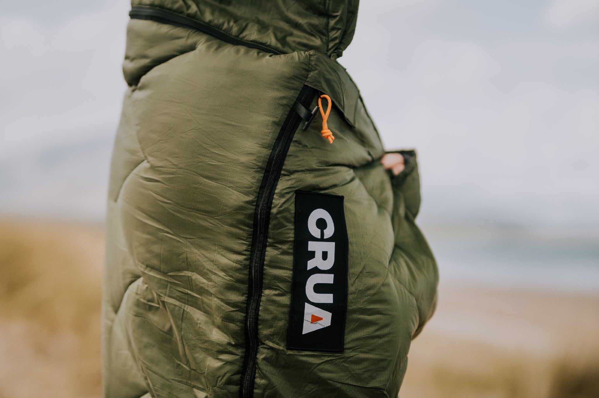 Person wrapped in Crua Graphene Sleeping Bag, fingers visible, blurred background.