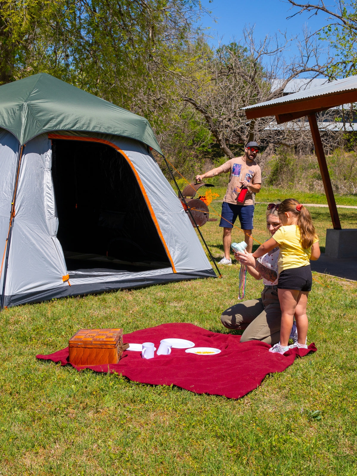 Crua Noir 6 Cabin Tent in a relaxed campsite scene with a dad accidentally flaring up the barbecue in the background while the family enjoys the outdoors