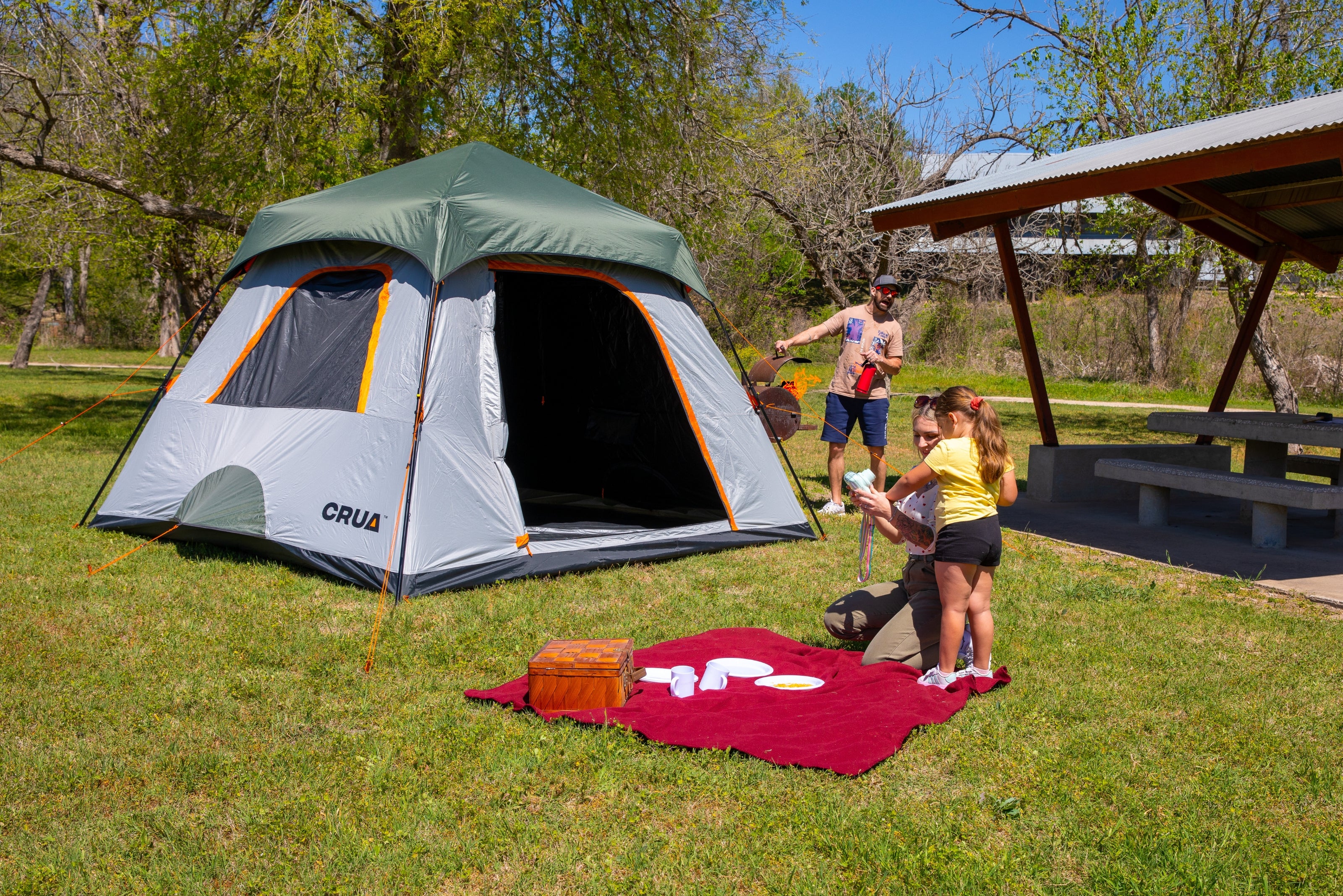 Crua Noir 6 Cabin Tent in a relaxed campsite scene with a dad accidentally flaring up the barbecue in the background while the family enjoys the outdoors